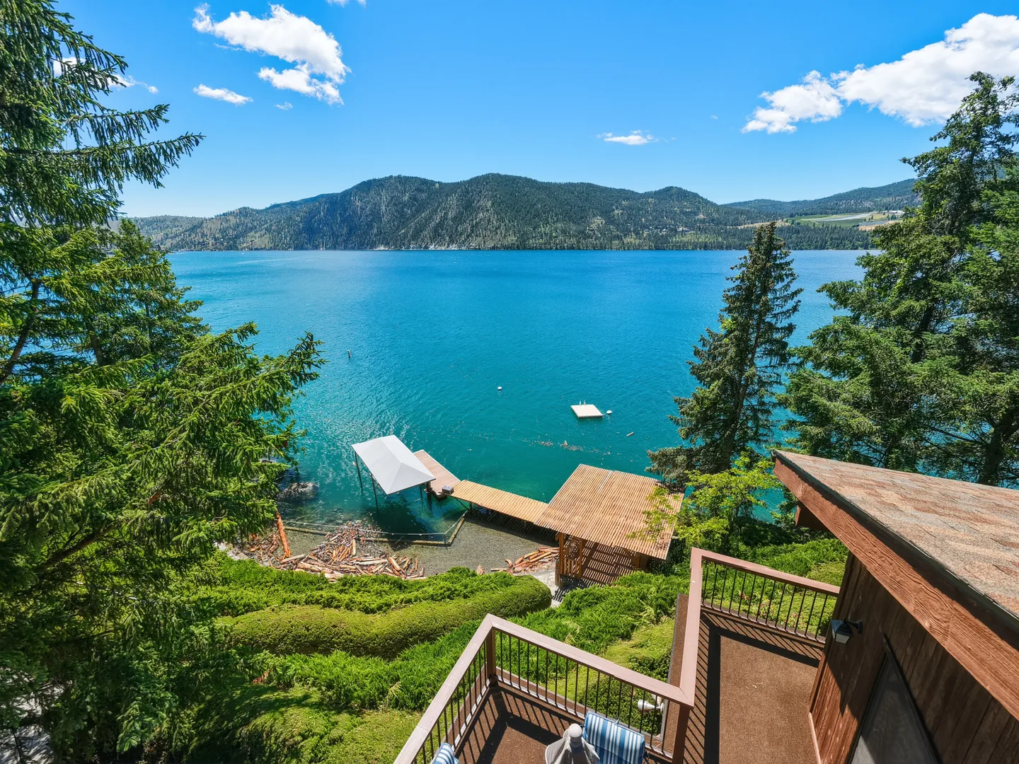 High-angle view from a house balcony overlooking a large blue lake surrounded by mountains and pine trees, with private docks below.