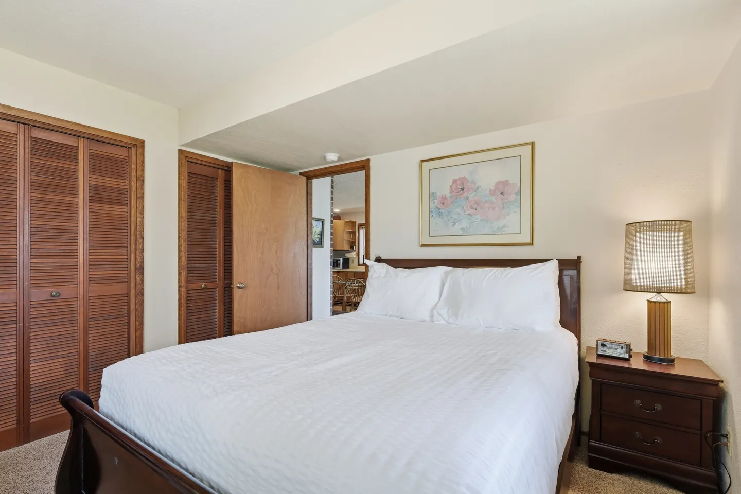 Bedroom featuring a wooden sleigh bed with white bedding, flanked by a nightstand with a lamp and closet doors.