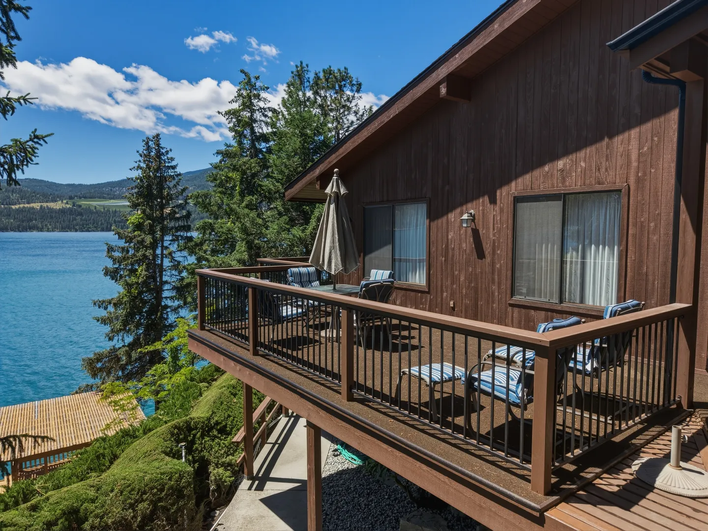 Elevated wooden deck with outdoor seating overlooking a large lake and pine trees.