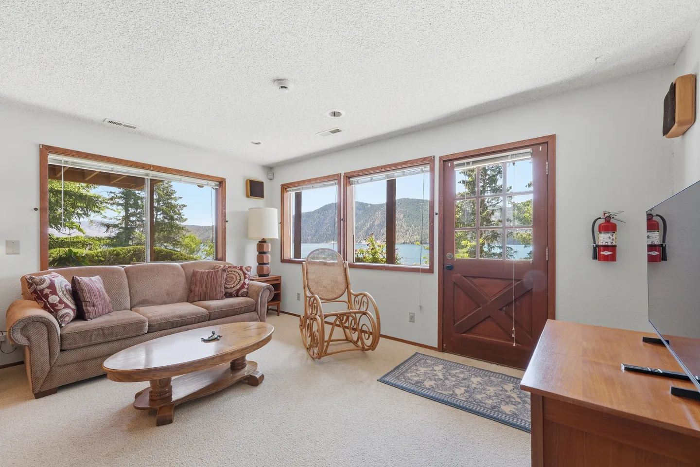 Living room with carpet, a sofa, rocking chair, coffee table, and windows showing lake and mountain views.