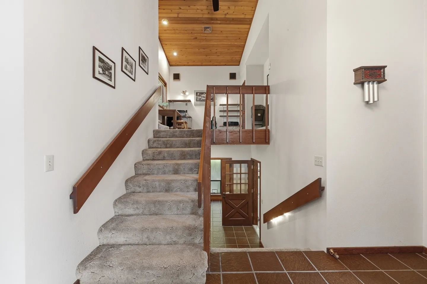 Carpeted split-level staircase with wood handrails leading up to an upper landing beneath a wood-paneled ceiling.