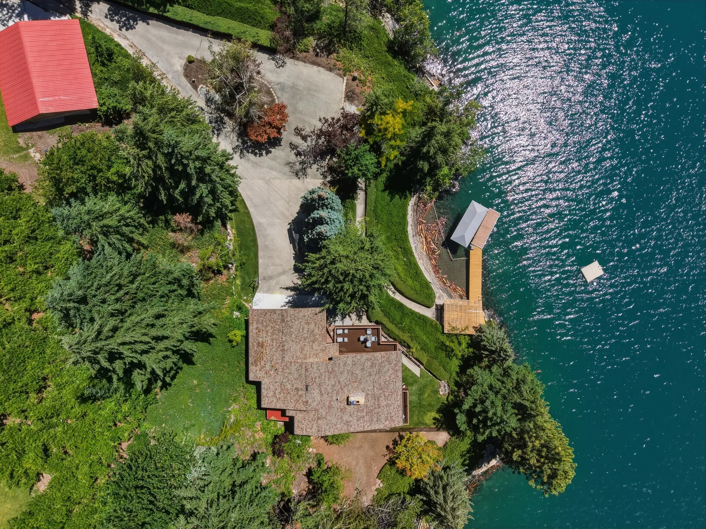Aerial view of a waterfront home surrounded by lush trees with a driveway, deck, and private boat dock.