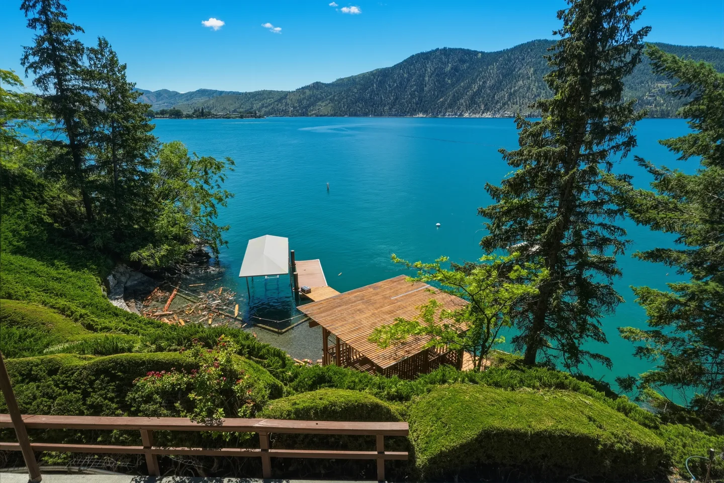 Elevated view overlooking vibrant blue lake waters, a private boat dock, a gazebo, and forested mountains in the distance.