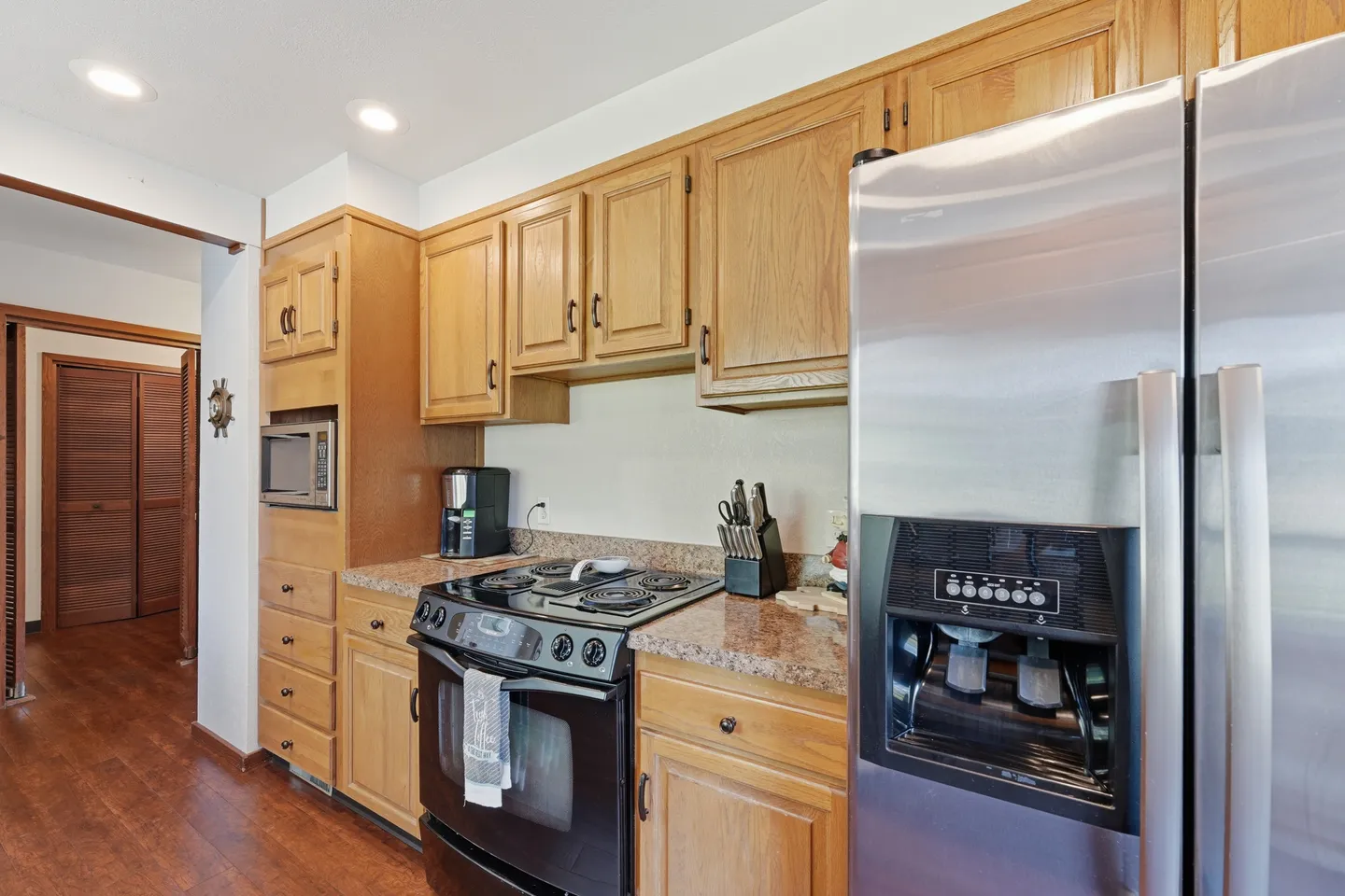 Kitchen with oak cabinetry, speckled laminate countertops, electric stove, built-in microwave, and stainless steel refrigerator.