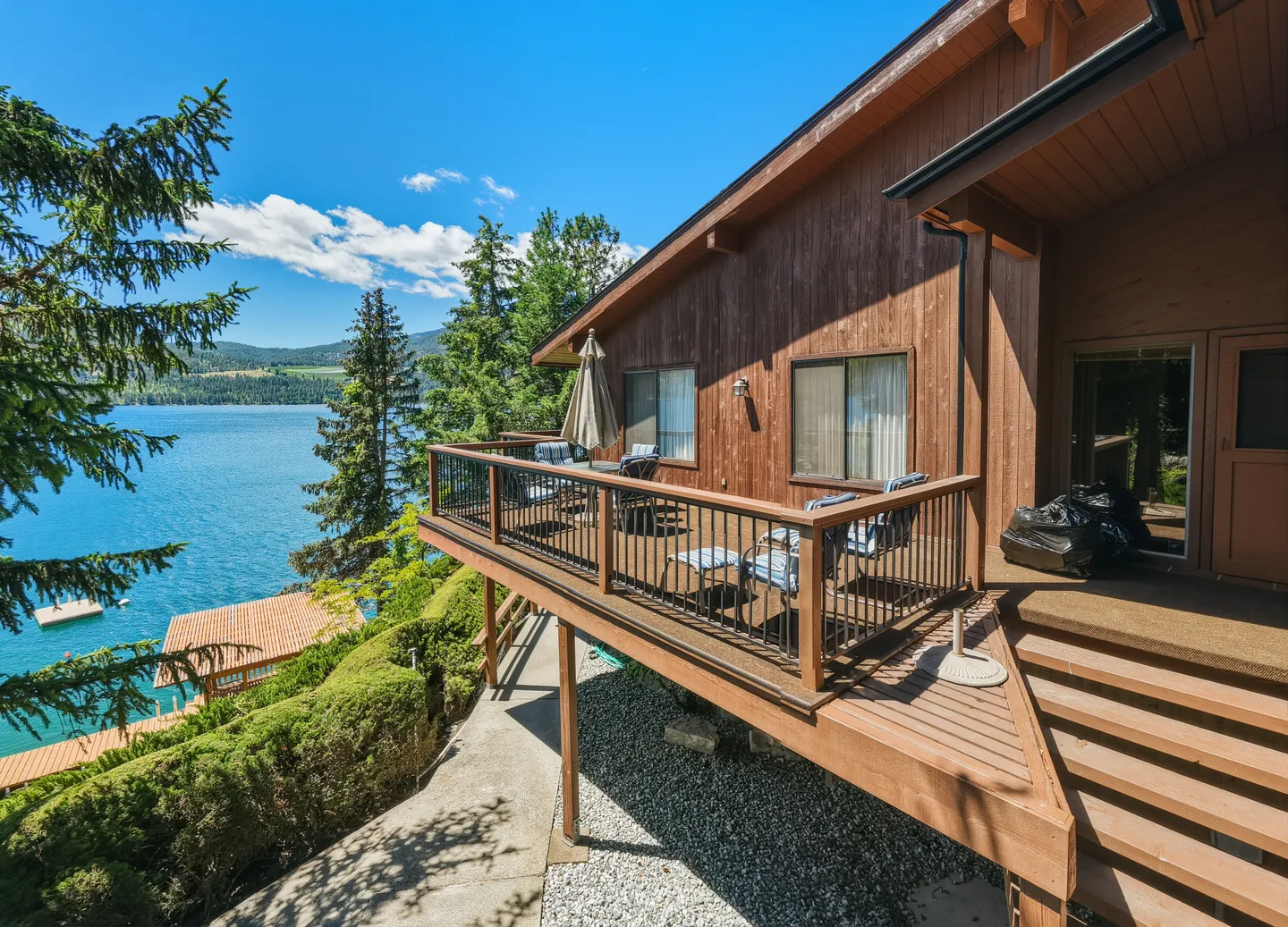 Exterior view of an elevated wooden deck with outdoor seating overlooking a large lake and mountains on a sunny day.