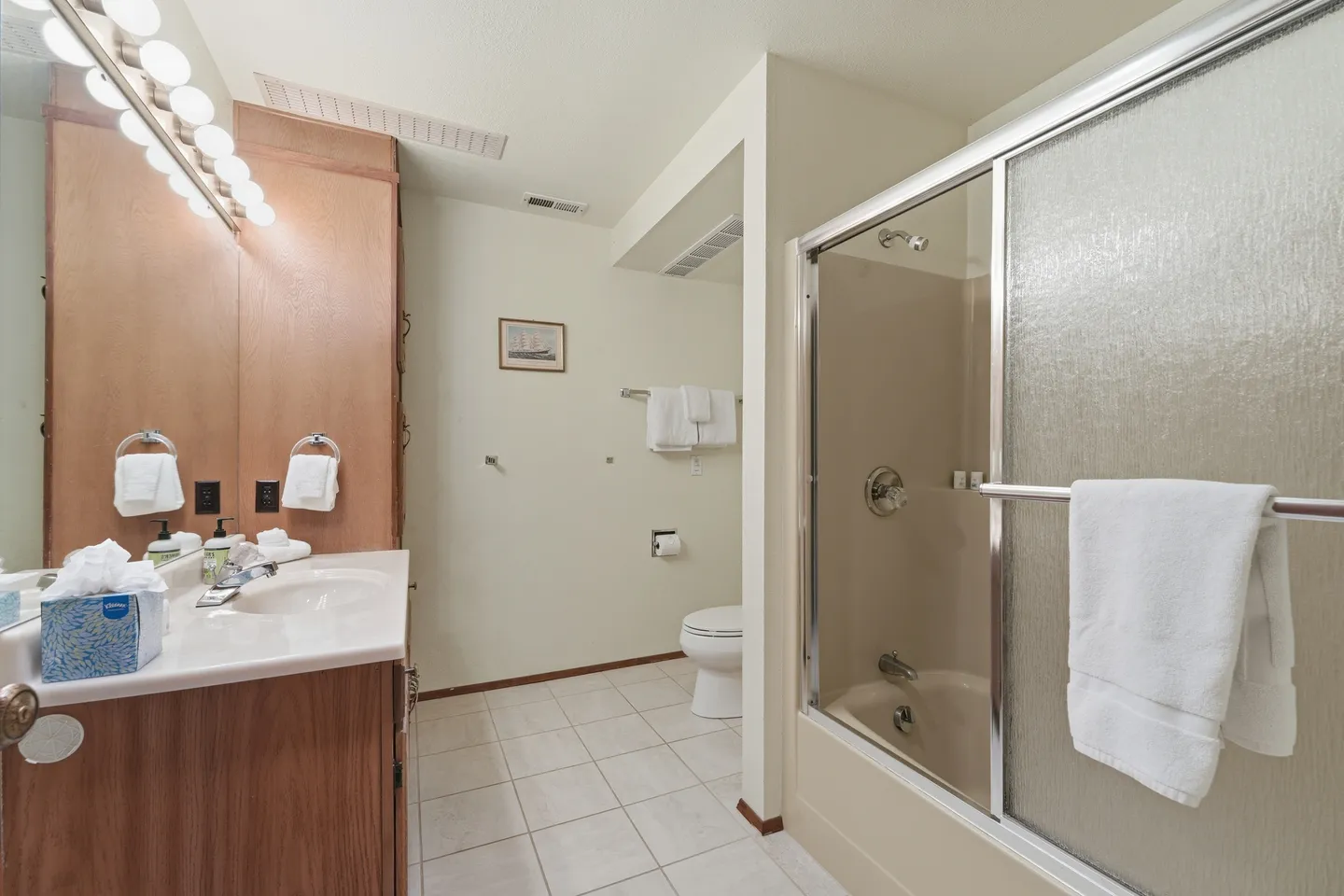 Bathroom with a double vanity and mirrors on the left, a toilet in the back, and a bathtub with sliding glass doors on the right.