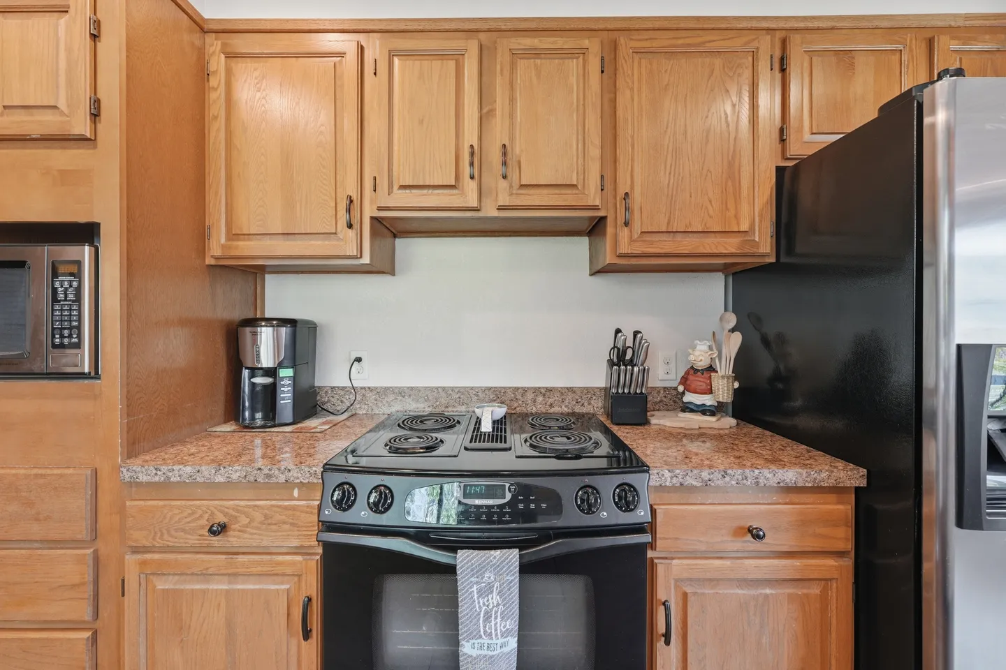 A close-up view of a kitchen stove with electric coil burners, wooden cabinets, and small appliances on the countertop.