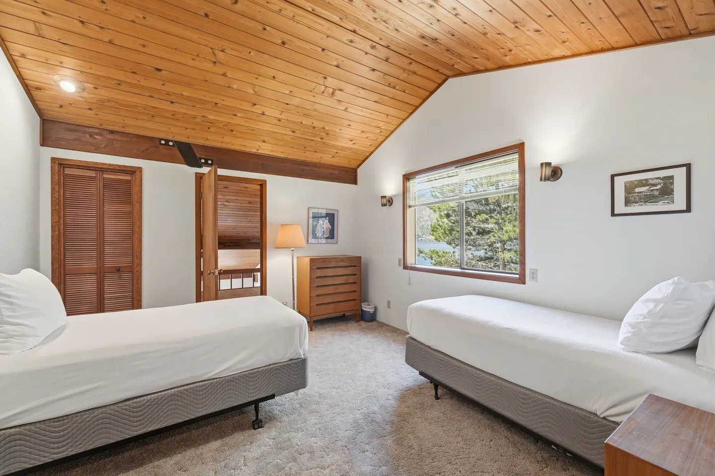 Bedroom featuring two twin beds, carpeted floors, and a wood-paneled vaulted ceiling with a window overlooking trees.