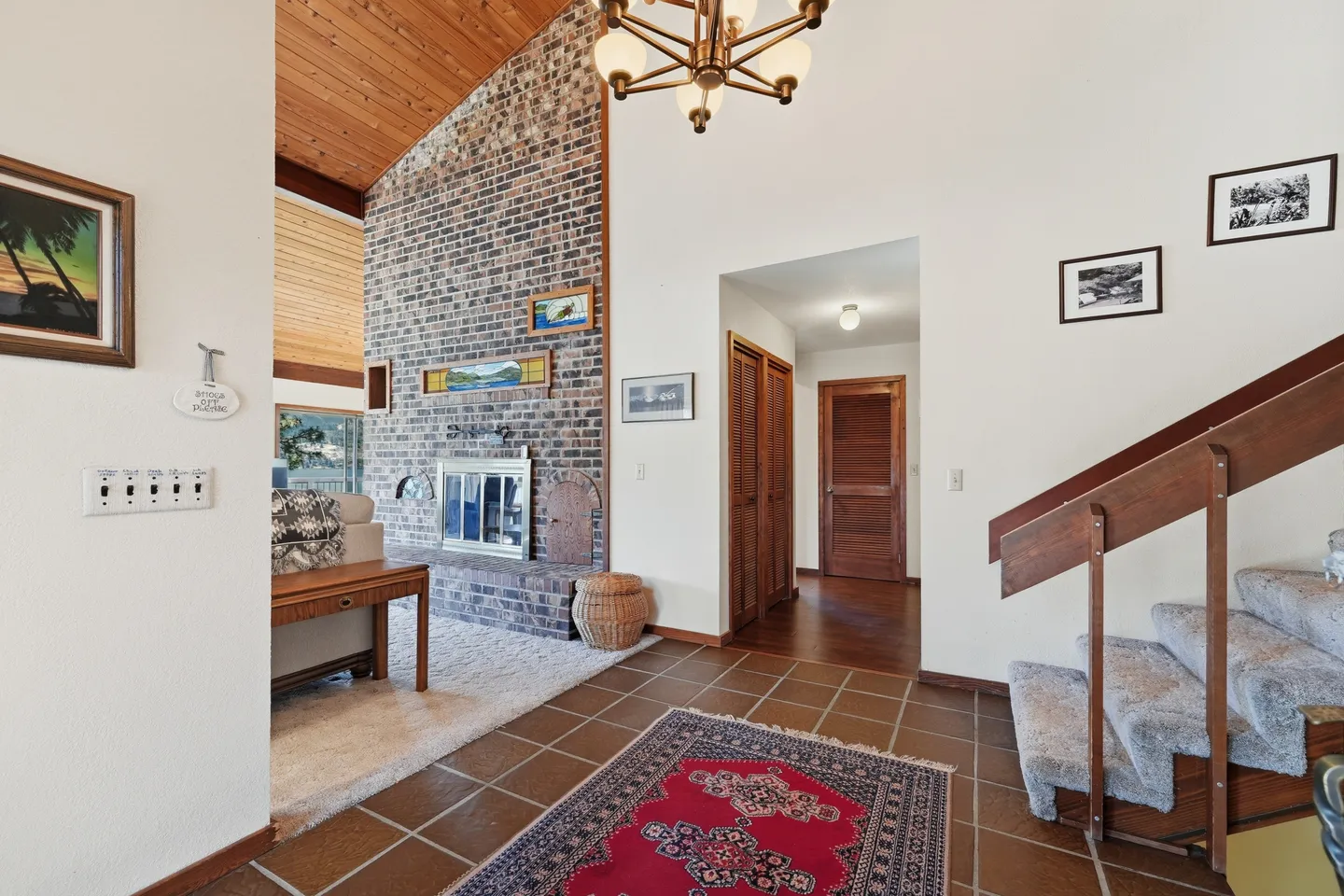 Tiled entryway leading into a living area with a tall brick fireplace and wood-paneled vaulted ceiling.