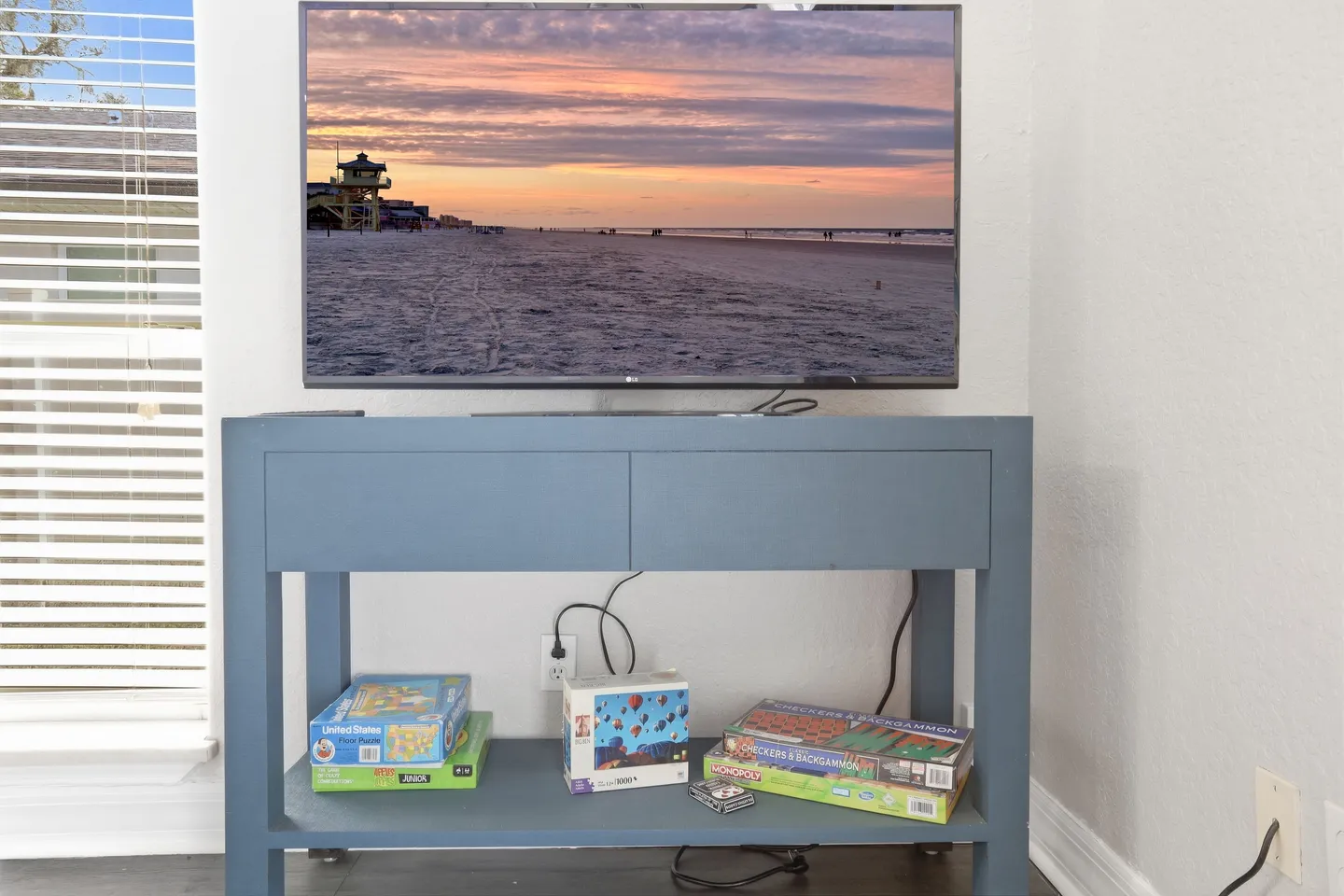 A flat-screen television displaying a beach scene sitting on a blue media console stocked with board games and puzzles.