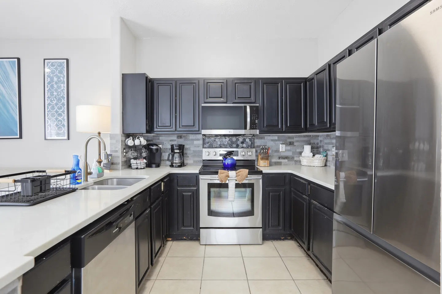 A kitchen with dark cabinetry, light countertops, tile flooring, and stainless steel appliances.