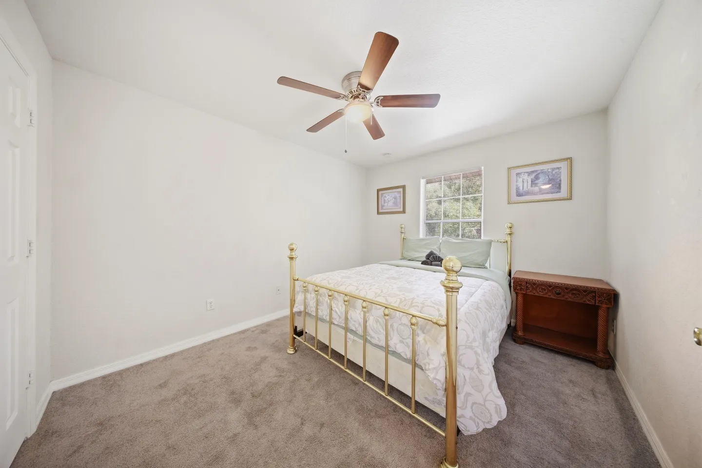 Bedroom with carpeted floor, brass metal bed frame, wooden nightstand, and ceiling fan.