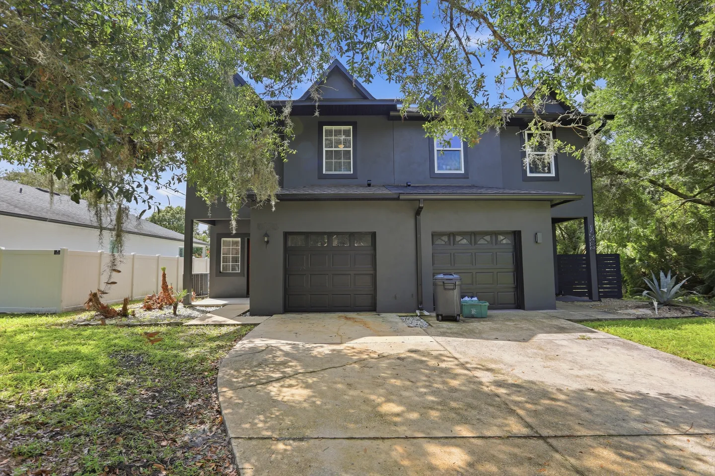 Exterior view of a two-story dark gray house with a wide driveway and attached garage doors.