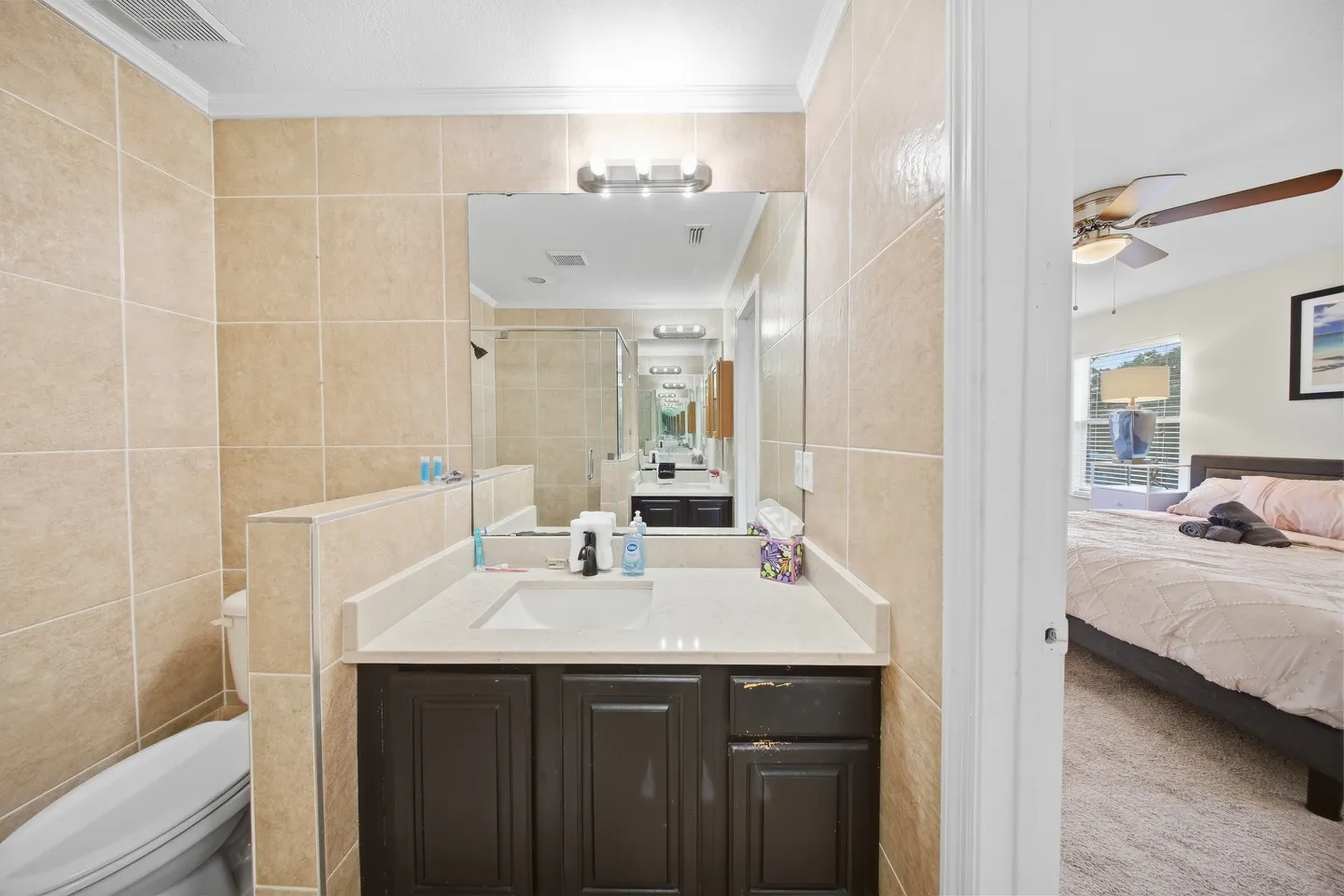 Bathroom with dark vanity, tiled walls, and mirror, adjacent to a carpeted bedroom.
