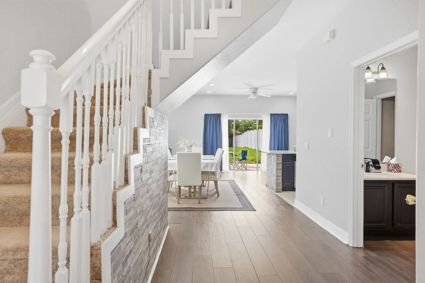 Hallway alongside a carpeted staircase leading toward a dining area and sliding glass doors to the backyard.