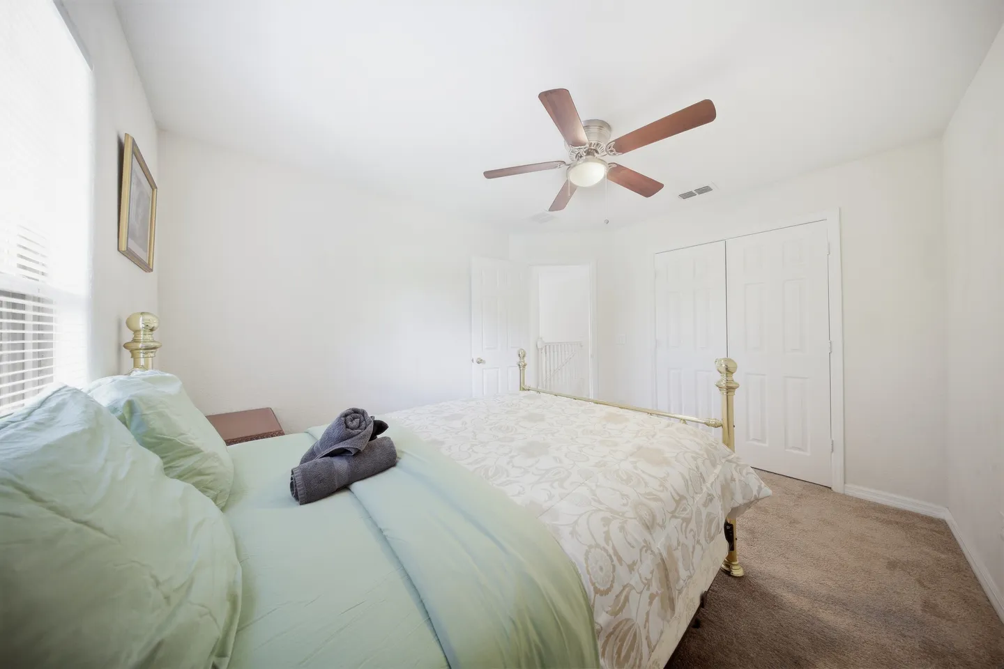 Bedroom with a brass bed frame, carpeted floor, ceiling fan, and white closet doors.