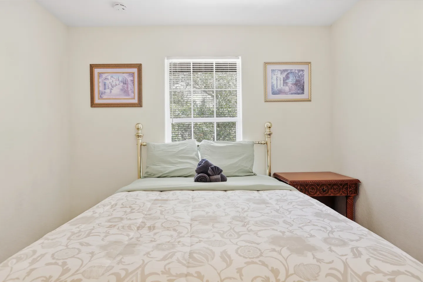 Bedroom featuring a brass-framed bed with floral bedding positioned under a window with blinds, flanked by two framed art prints.