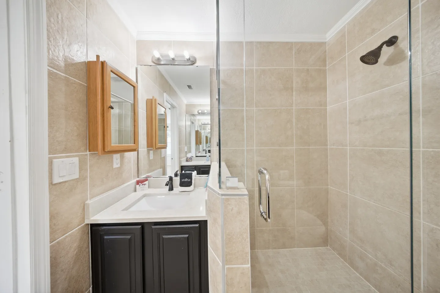 Bathroom with a dark vanity cabinet, a walk-in shower with beige tile, and a glass partition.