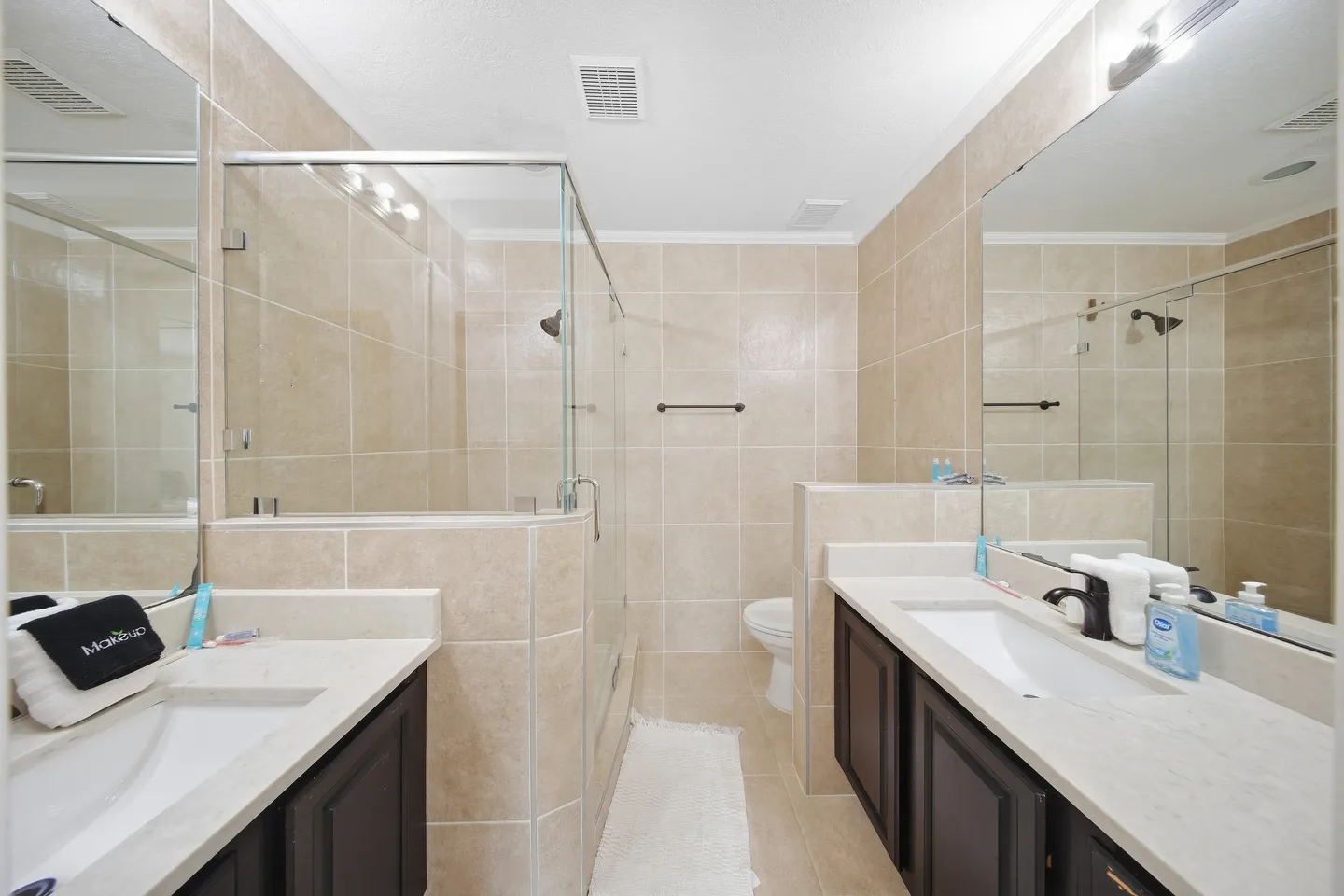 Bathroom with dual vanities with dark cabinets on opposite walls and a walk-in glass shower in the center.