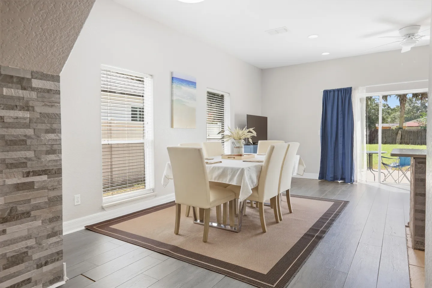 Dining area with a rectangular table, upholstered chairs, area rug, wood-look flooring, and sliding glass doors leading outside.
