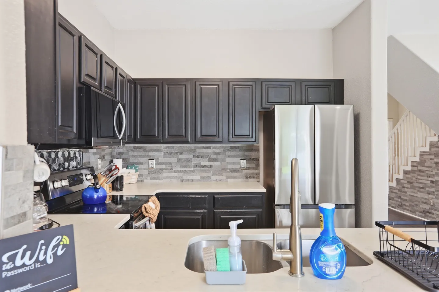 Kitchen with dark cabinetry, light countertops, stainless steel refrigerator, and foreground sink.