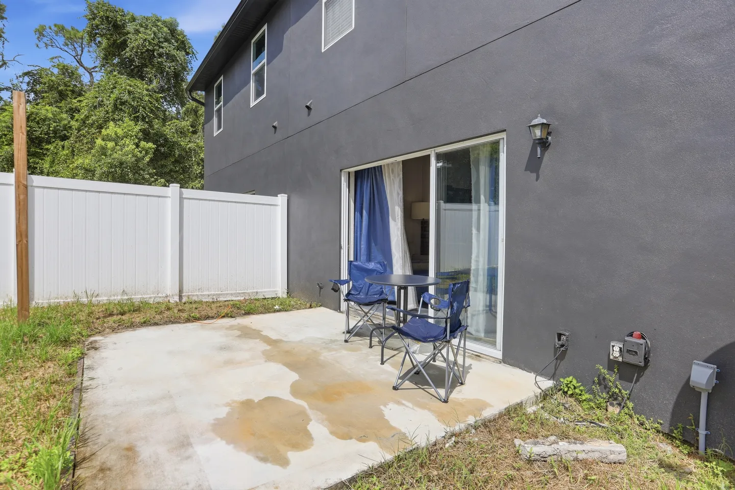 Concrete back patio with two folding camp chairs, a small table, and sliding glass doors leading into the home.