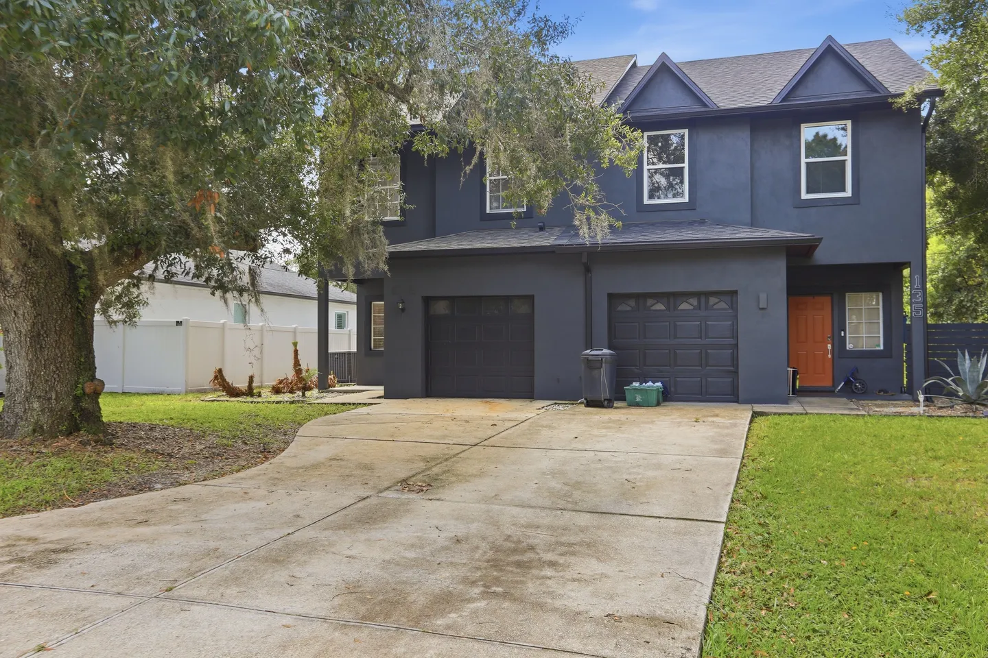 Exterior view of a two-story dark grey house with a concrete driveway and two garage doors.