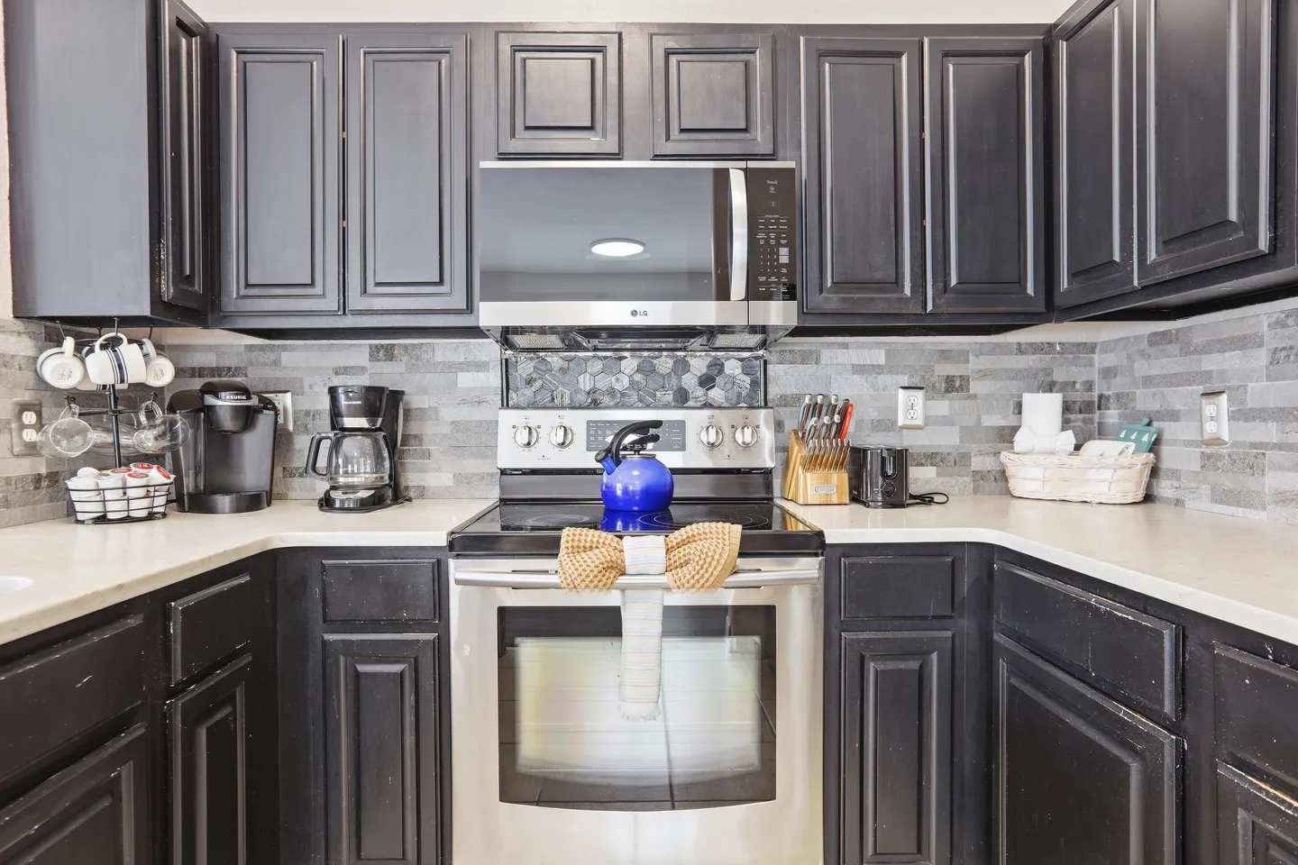 Kitchen counter area with dark paneled cabinets, a stainless steel electric stove and oven, built-in microwave, and tiled backsplash.