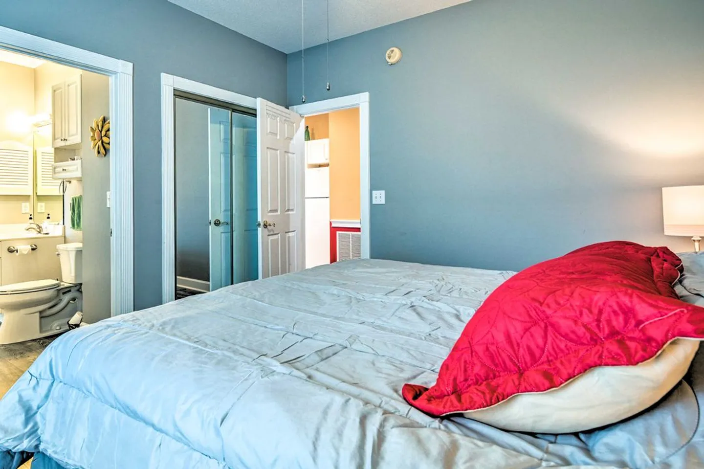 Bedroom with blue walls, a bed in the foreground, and doorways leading to a bathroom and closet.