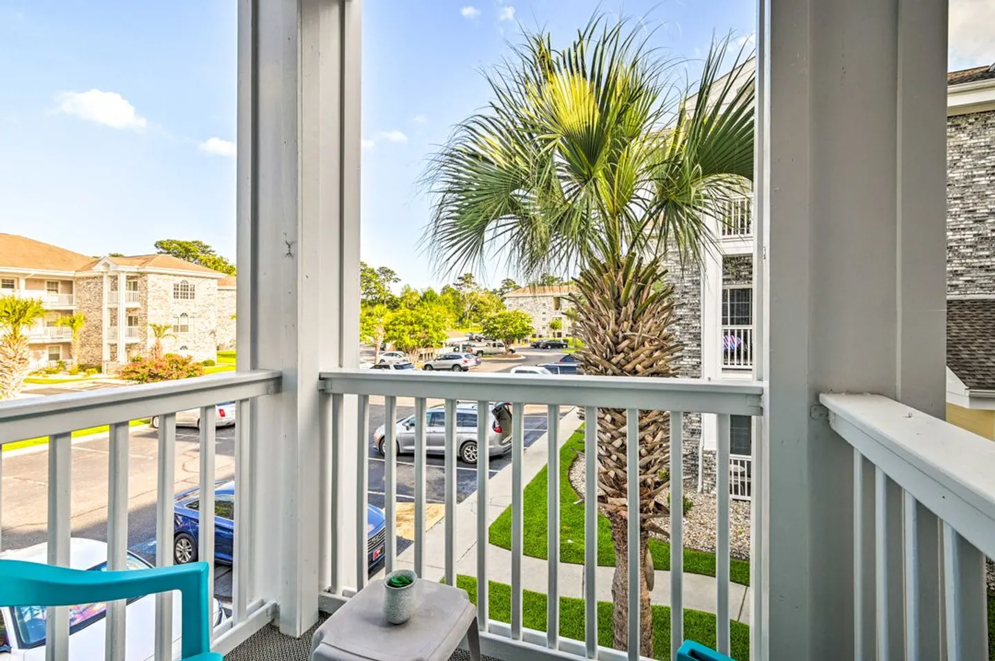 Balcony view overlooking a parking lot, residential buildings, and palm trees under a blue sky.