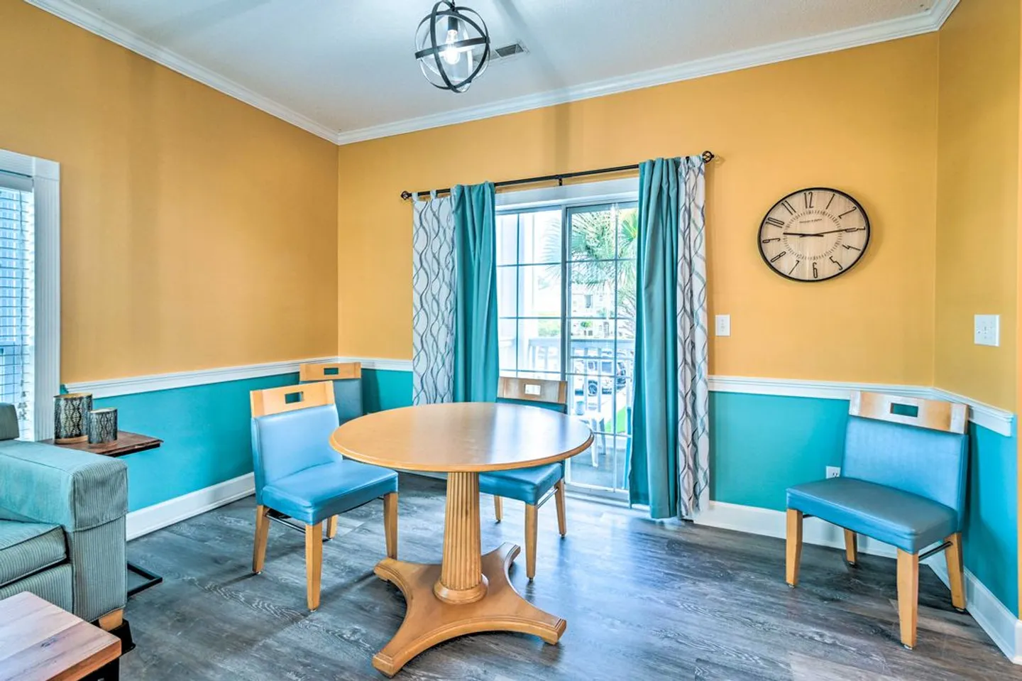 Dining area with a round wooden table, blue chairs, two-tone yellow and turquoise walls, and sliding glass doors.