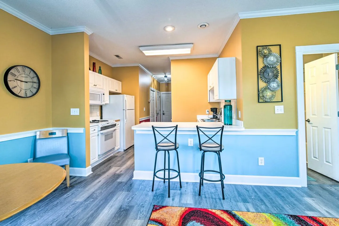 Kitchen and breakfast bar with two tall chairs, white appliances, and two-tone yellow and light blue walls.