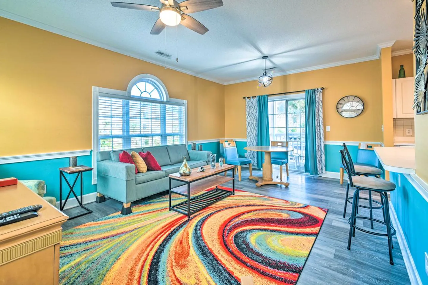 Living and dining area featuring yellow and turquoise walls, a patterned swirl rug, blue sofa, and glass sliding doors.