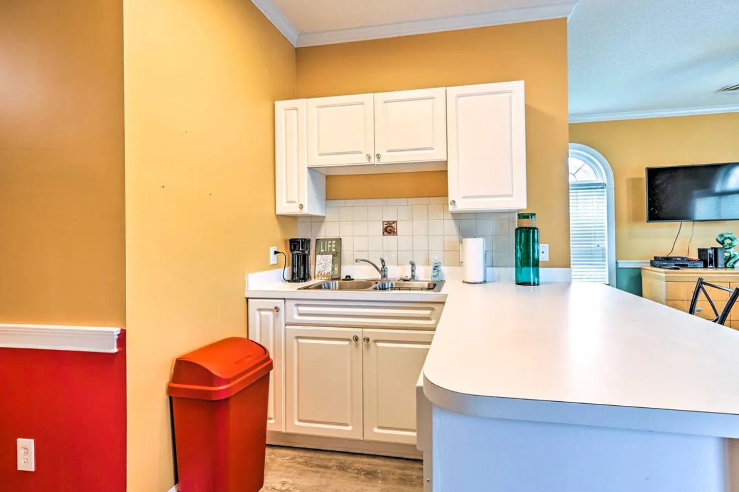 Wet bar and counter area with white cabinetry, a sink, and a coffee maker in a yellow and red room.