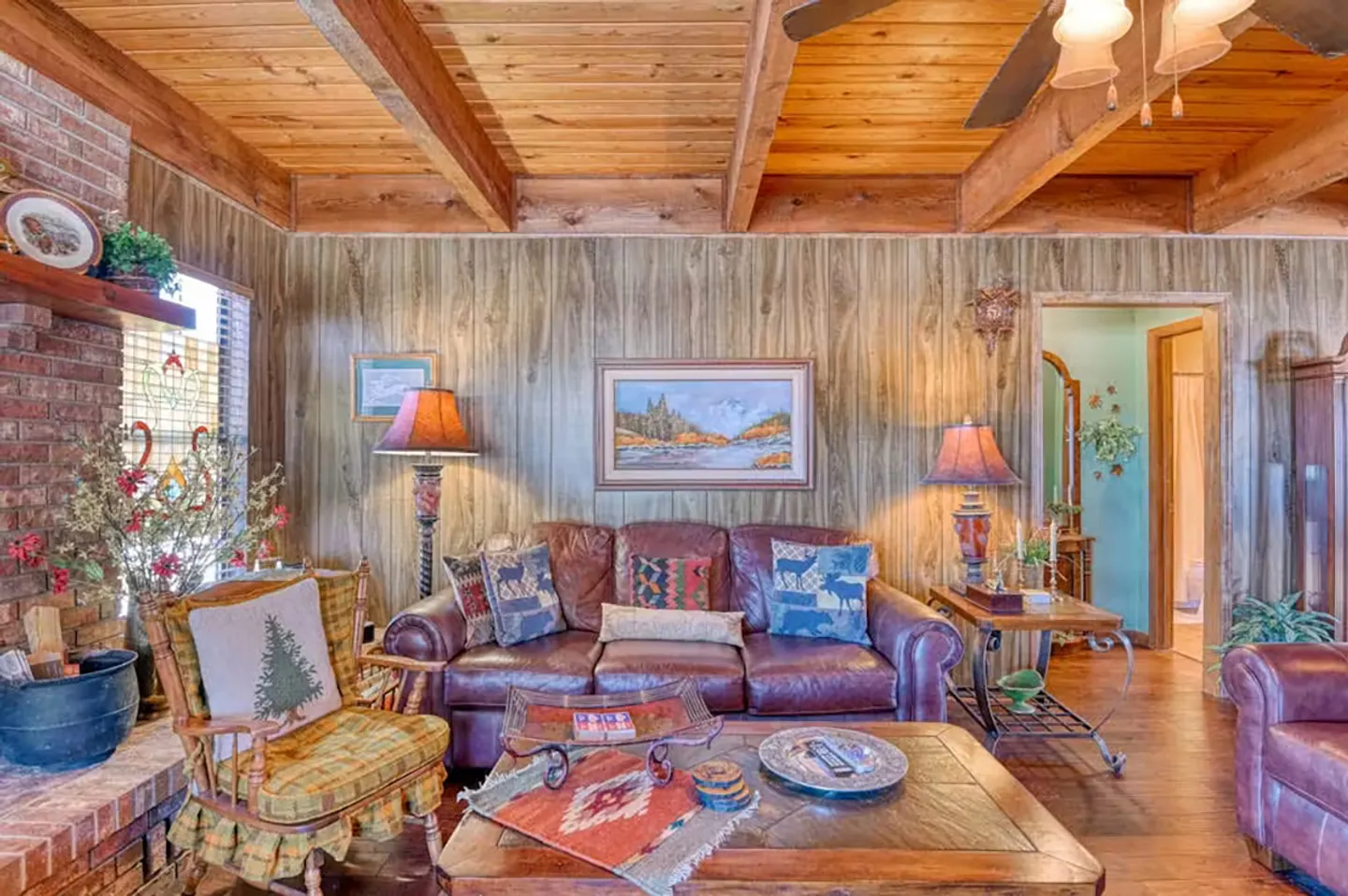 Living room with wood paneling, exposed ceiling beams, leather sofa, and a brick fireplace.