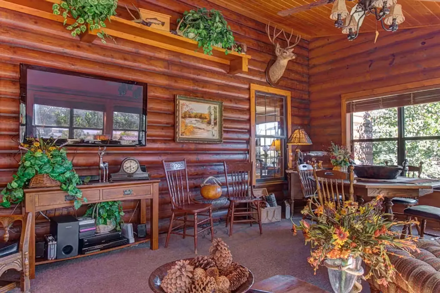 Rustic log cabin living and dining area featuring a mounted flat-screen TV, wooden furniture, and log-paneled walls.