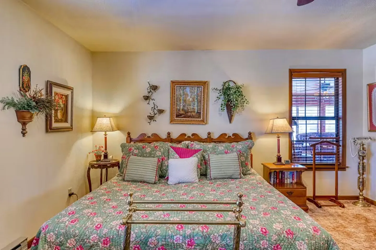 Bedroom featuring a bed with a floral quilt, wooden headboard, side tables with lamps, and decorated walls.