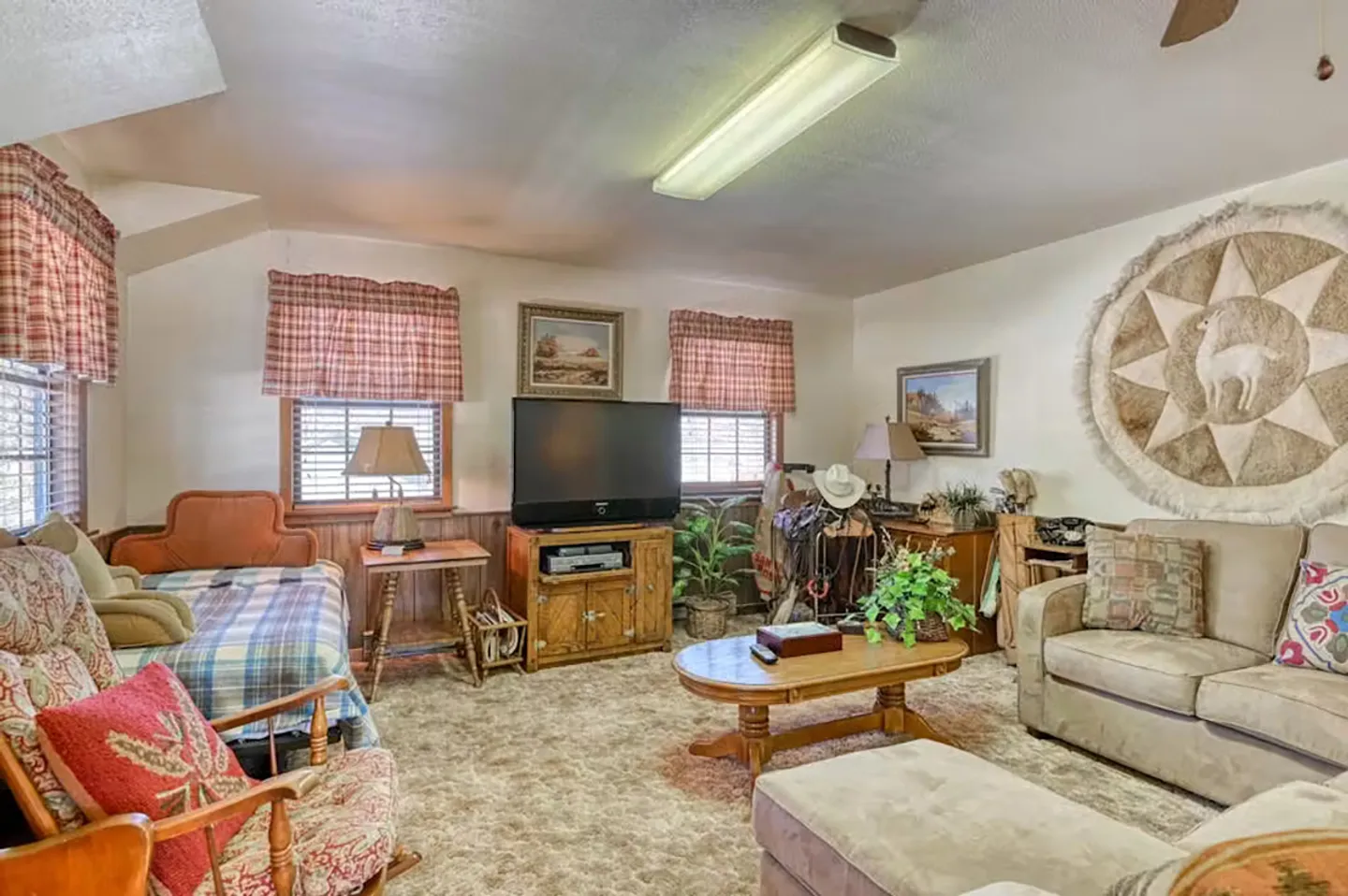 Living room with carpet, a sofa, coffee table, rocking chair, TV on a stand, and rustic wall decor.