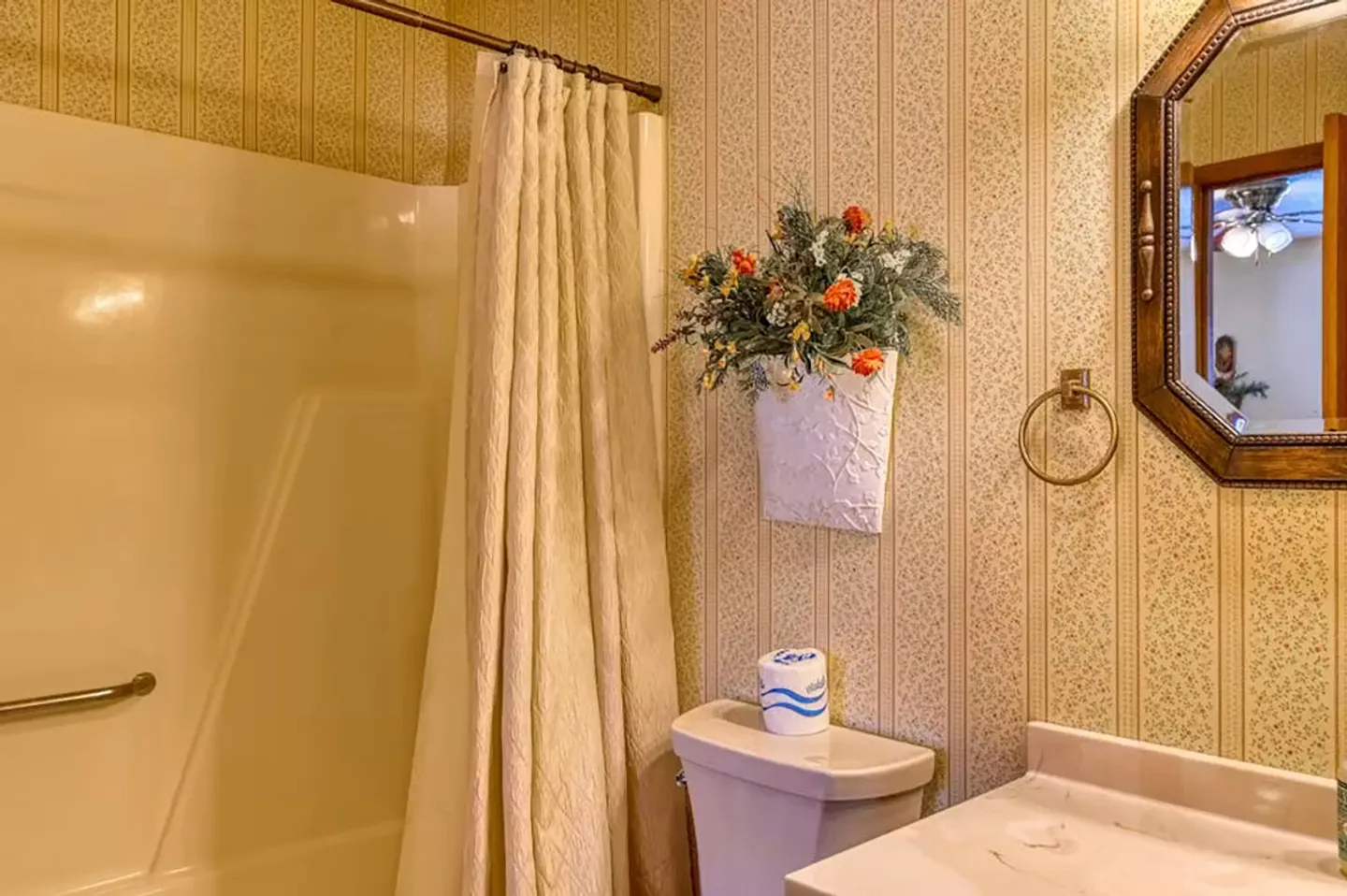 Bathroom featuring patterned wallpaper, a toilet, a vanity counter, a wall mirror, and a bathtub with shower curtain.
