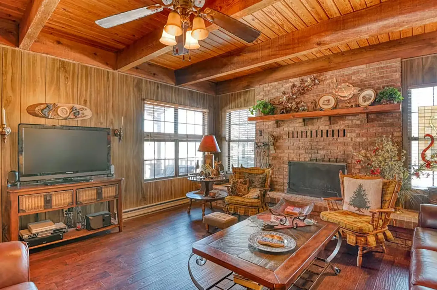 Living room with wood-paneled walls, exposed wood ceiling beams, a brick fireplace, and an entertainment center.