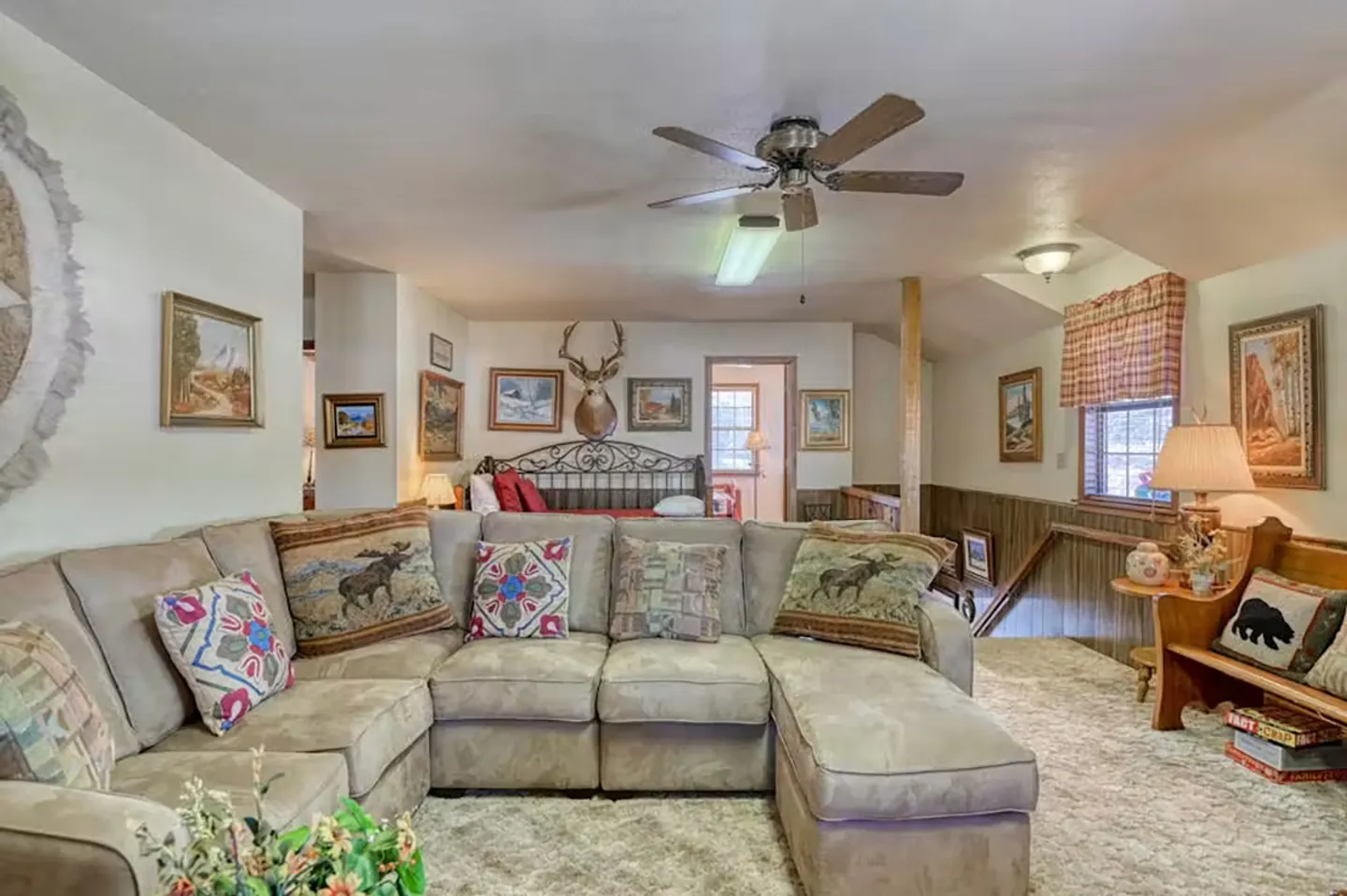Upstairs living space featuring a large sectional sofa, carpeted floor, ceiling fan, and a view into an adjacent sleeping area.