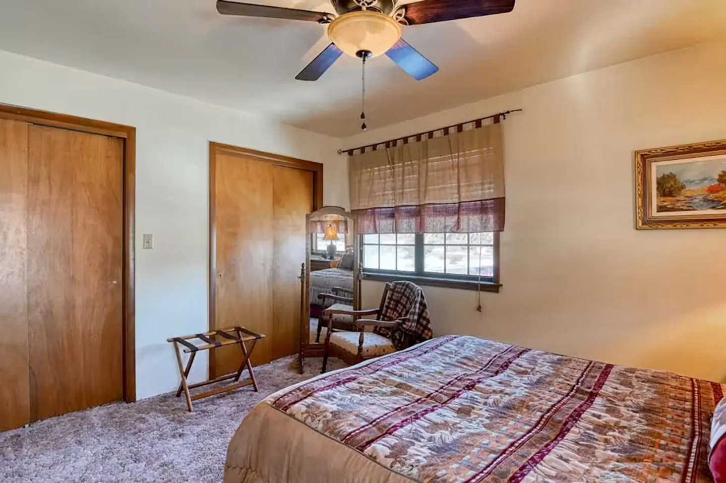Bedroom featuring a made bed with a patterned comforter, carpet flooring, a ceiling fan, and wooden closet doors.