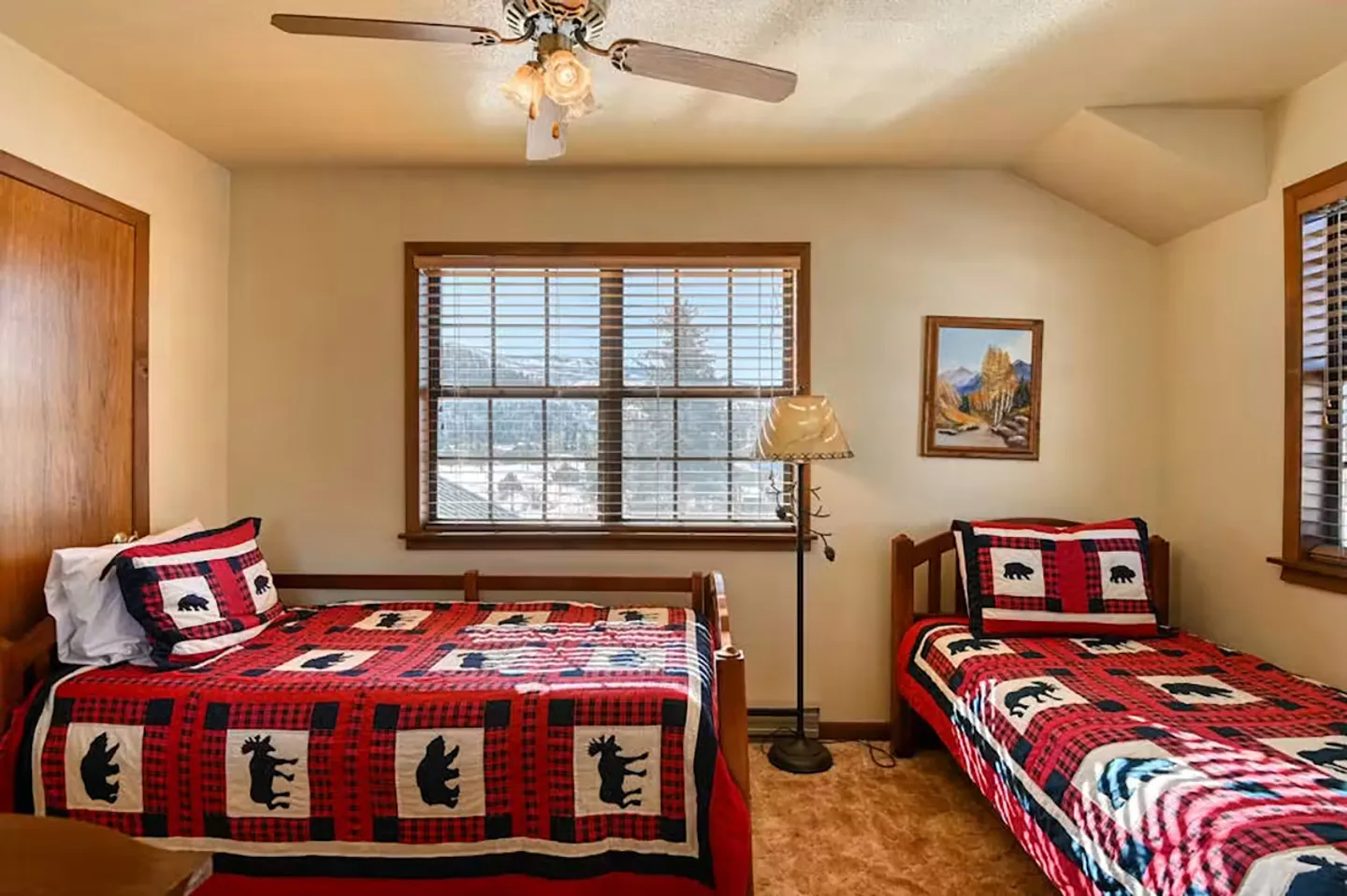 Bedroom with two single beds featuring moose-patterned red and black quilts, a window with blinds, and a ceiling fan.