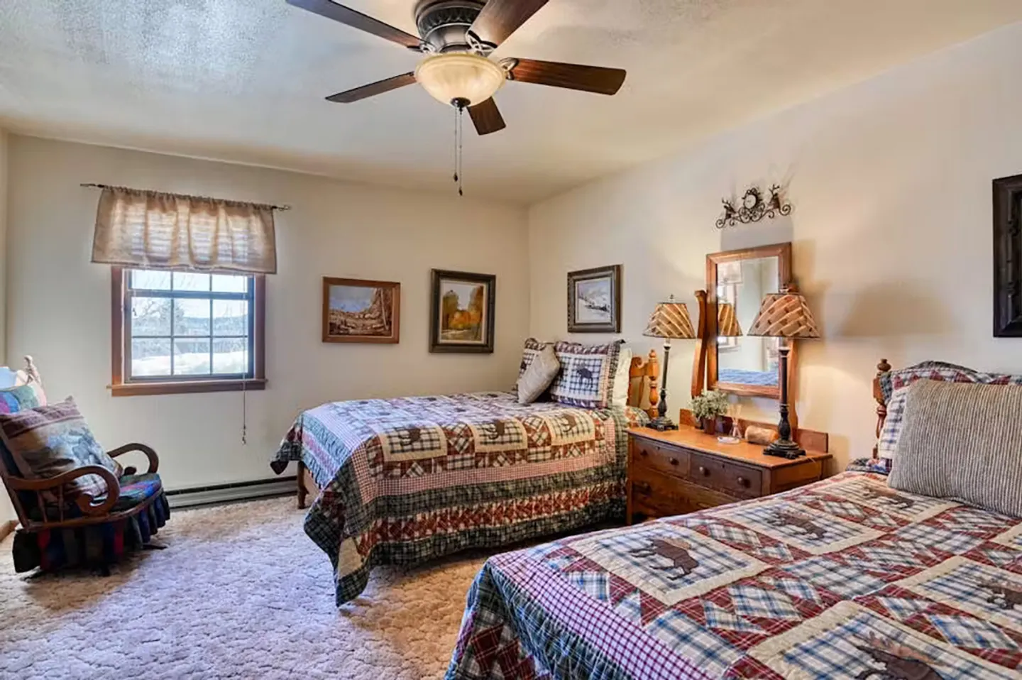 Bedroom with two beds made with rustic patchwork quilts, a wooden nightstand with lamps, and a window.