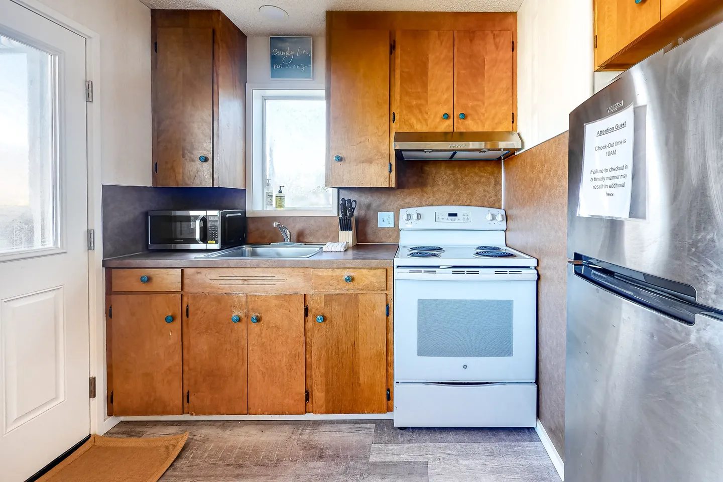 Kitchen with wooden cabinets, laminate countertops, a stainless steel sink, a white electric range, a microwave, and a stainless steel refrigerator.