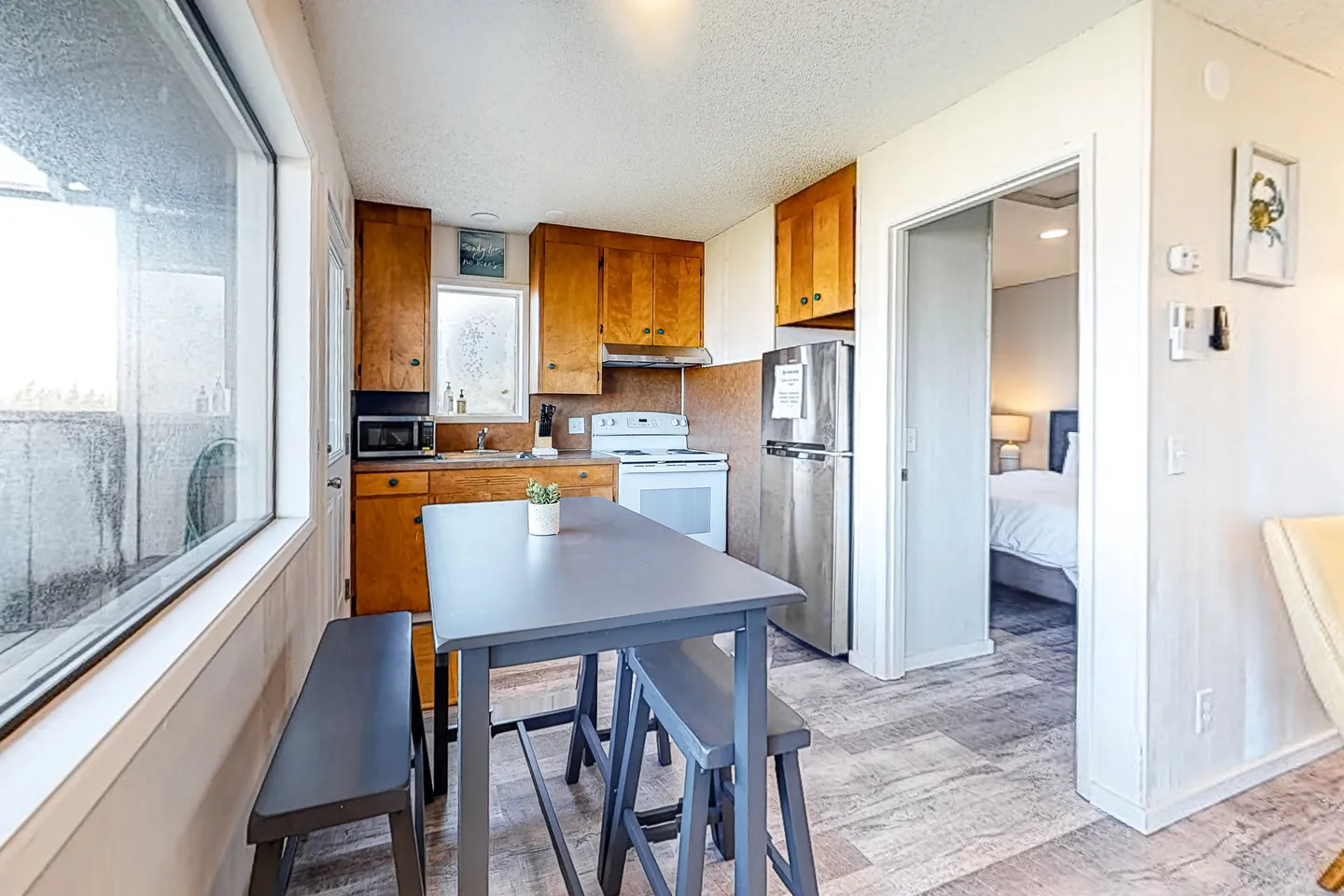 Kitchenette and dining area with grey dining table and bench seating, adjacent to an open bedroom doorway.