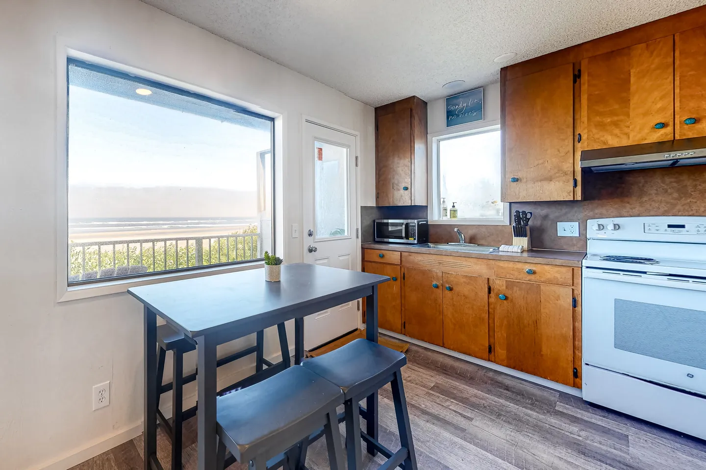 Kitchen and dining nook featuring wooden cabinets, a white stove, and a small dining table next to a large picture window with an ocean view.