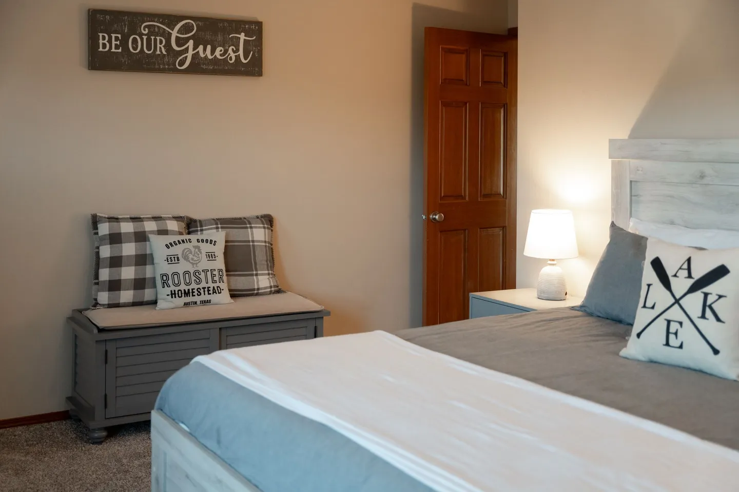 Bedroom featuring a made bed with accent pillows, a bedside lamp on a nightstand, and a storage bench along the wall.