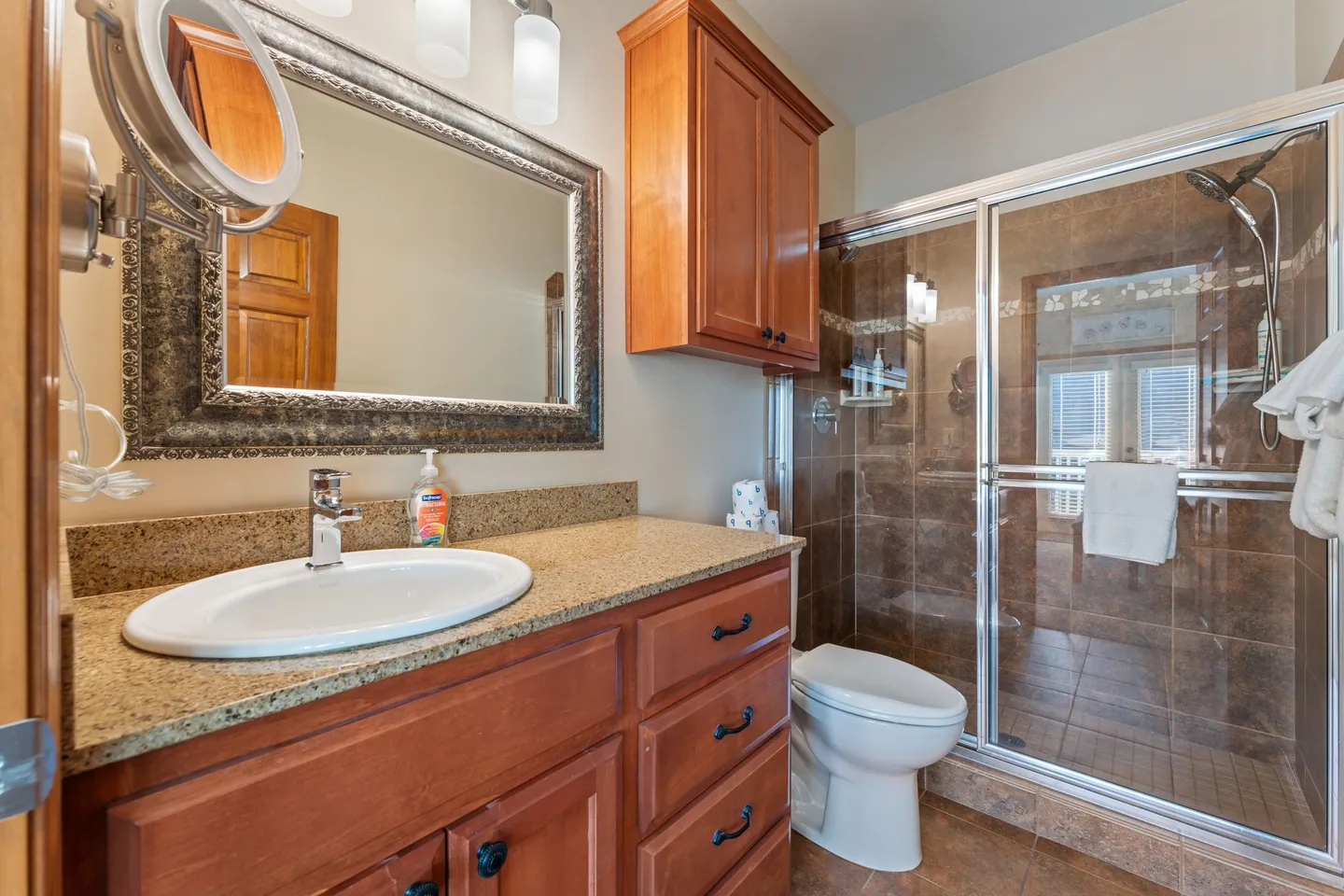Bathroom featuring a wood vanity with speckled countertop, framed mirror, toilet, and glass-enclosed tiled walk-in shower.