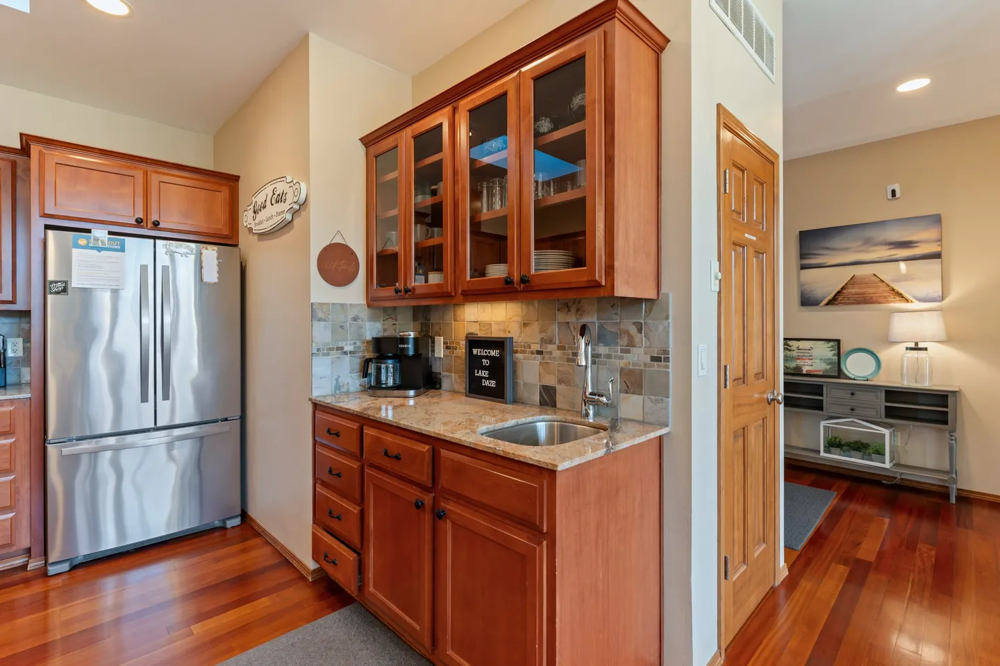 Wet bar area featuring wood cabinets with glass-front uppers, a small sink, and a coffee maker next to a stainless steel refrigerator.